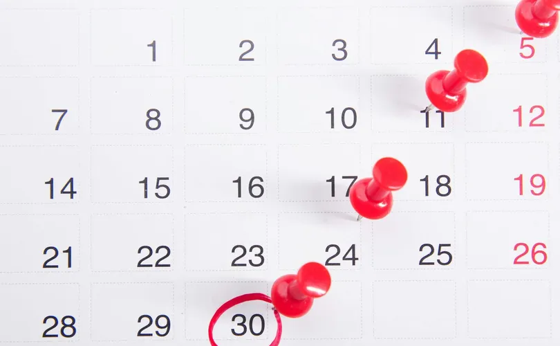 Close-up of a calendar with red push pins marking