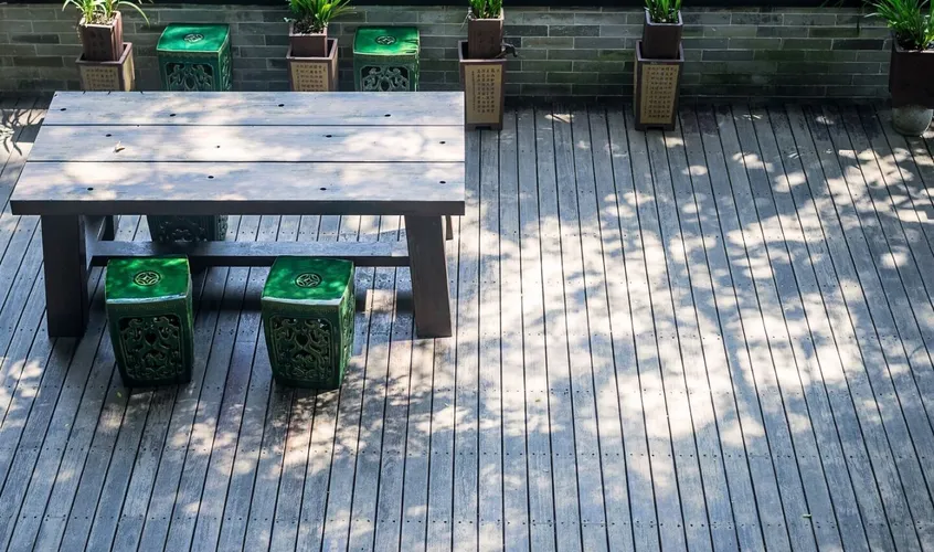 Timber deck seating area with a wooden table, ceramic stools and potted plants
