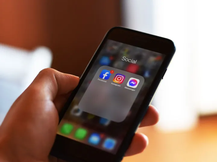 A hand holding a smartphone showing Facebook, Instagram and Messenger apps