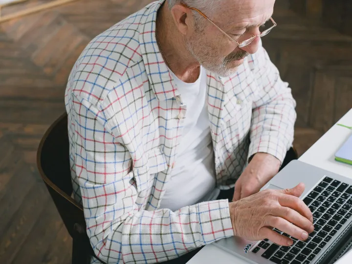 An older man in a checked shirt typing on a laptop