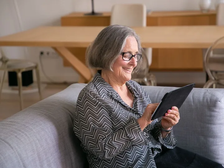 An older woman smiling as she reads a website on a tablet at home
