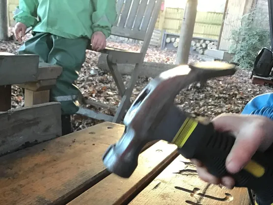 A child hammering a nail into a slice of log at the woodwork bench