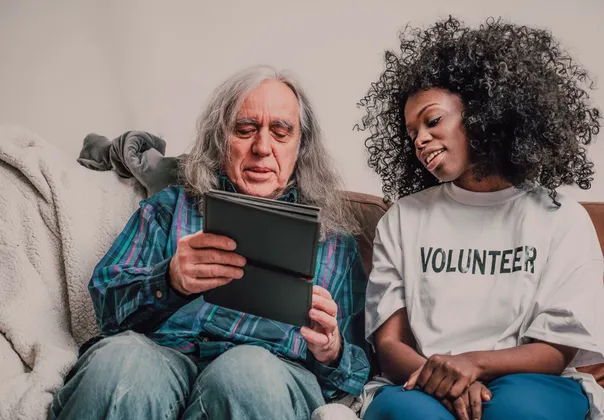 Young volunteer helping an older man use a tablet