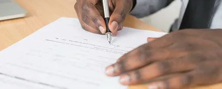 Person Holding Gray Twist Pen and White Printer Paper on Brown Wooden Table