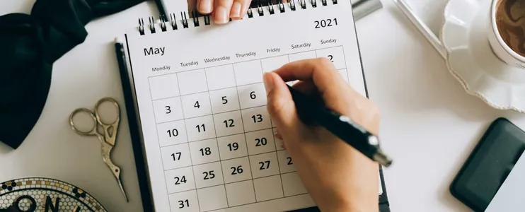 Top view of hands using a planner with coffee and accessories, focused on May 2021 calendar.