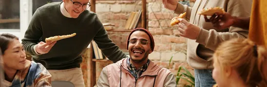 A joyful group of diverse friends enjoying pizza together in a cozy indoor setting.