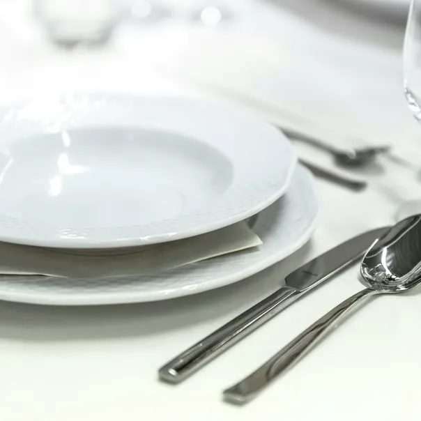 Elegant dining table with white porcelain plates and silver cutlery elegantly arranged.
