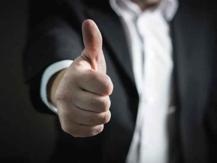 A close-up of a man's thumbs up gesture, symbo