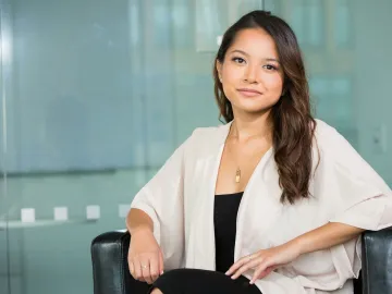 A professional Asian businesswoman sitting confidently in a modern office setting.
