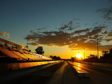 A stunning sunset illuminates an empty racetrack with bleachers, highlighting the sky and track lines.