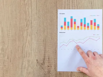 Hand analyzing business graphs on a wooden desk, f
