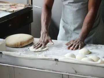 A baker in an indoor kitchen kneading dough for br