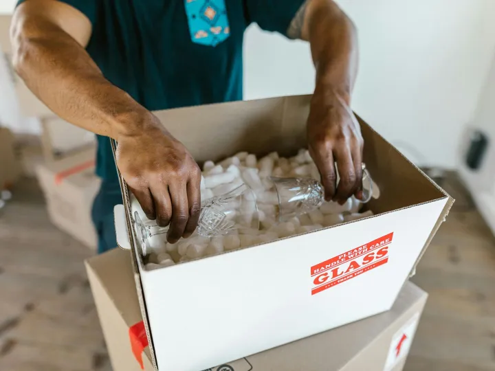 Hands carefully packing glassware into a cardboard