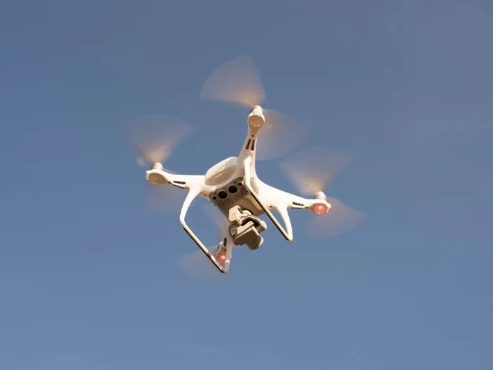 A white drone in flight against a clear blue sky
