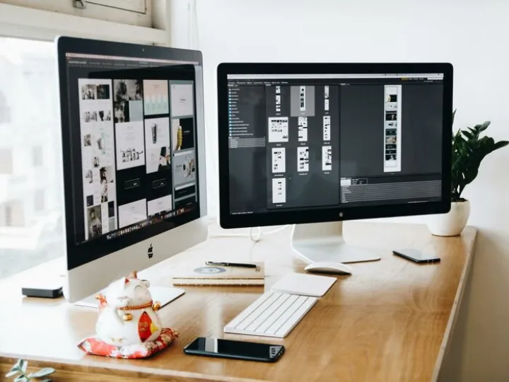 Two Imac'S With Keyboard and Phones On Desk