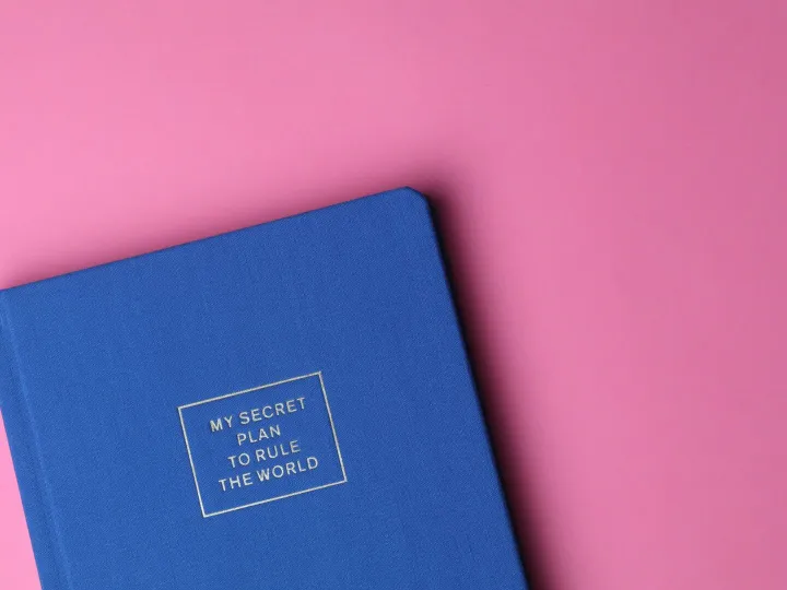 Stylish blue notebook on pink background with inspiring text cover.