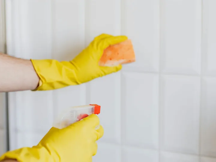 A person wearing yellow gloves cleans bathroom til