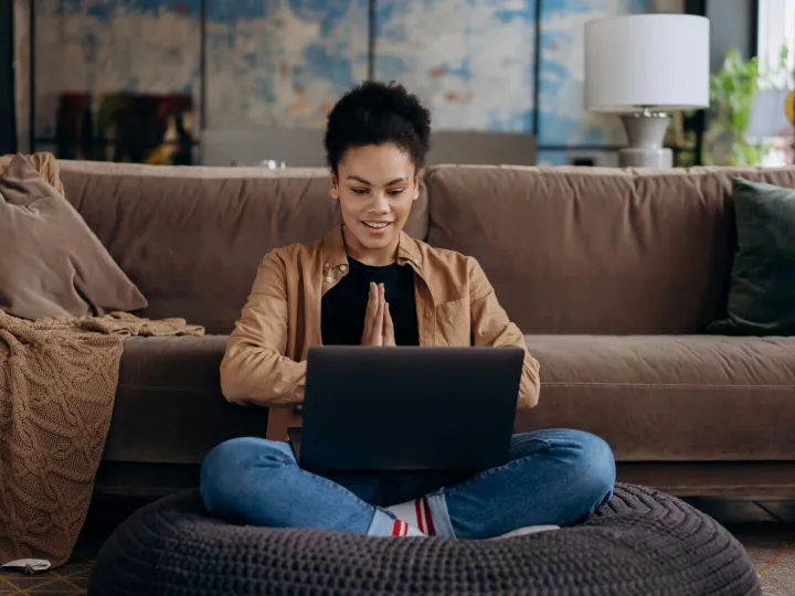 A smiling young woman sits cross-legged on a pouf,
