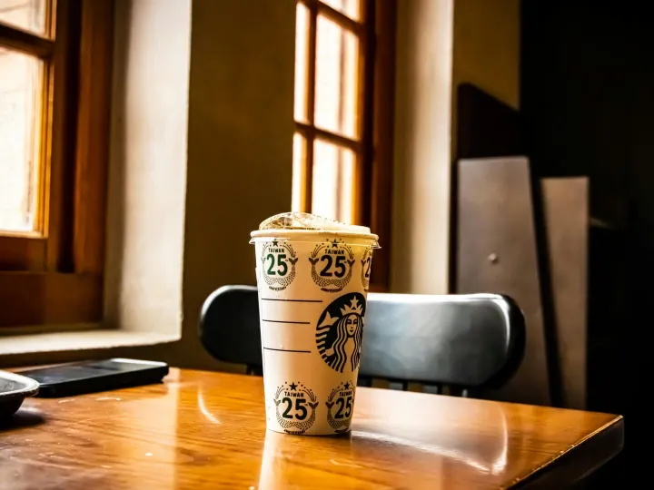 A Starbucks cup on a wooden table near a window in