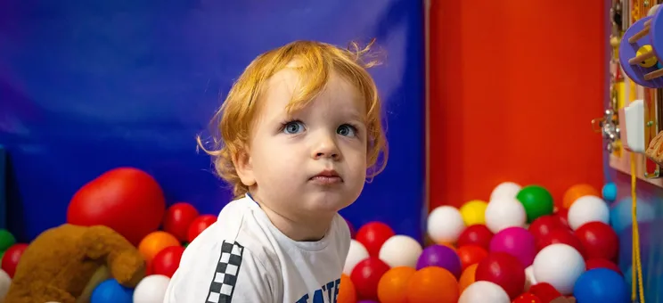 Toddler sitting in a colourful soft play ball pit